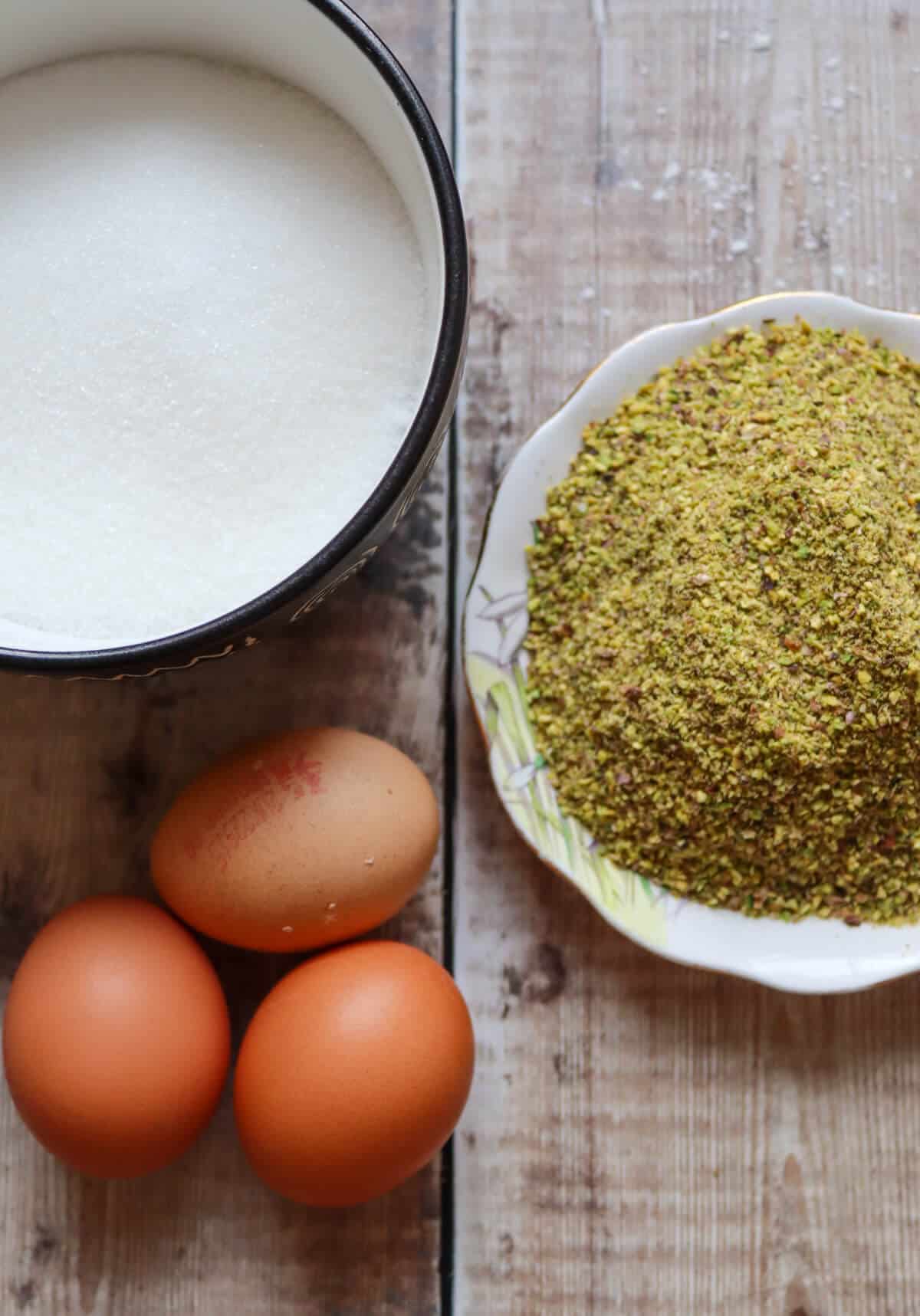 The ingredients for pistachio meringue on a table. Sugar, eggs and ground pistachio nuts. 