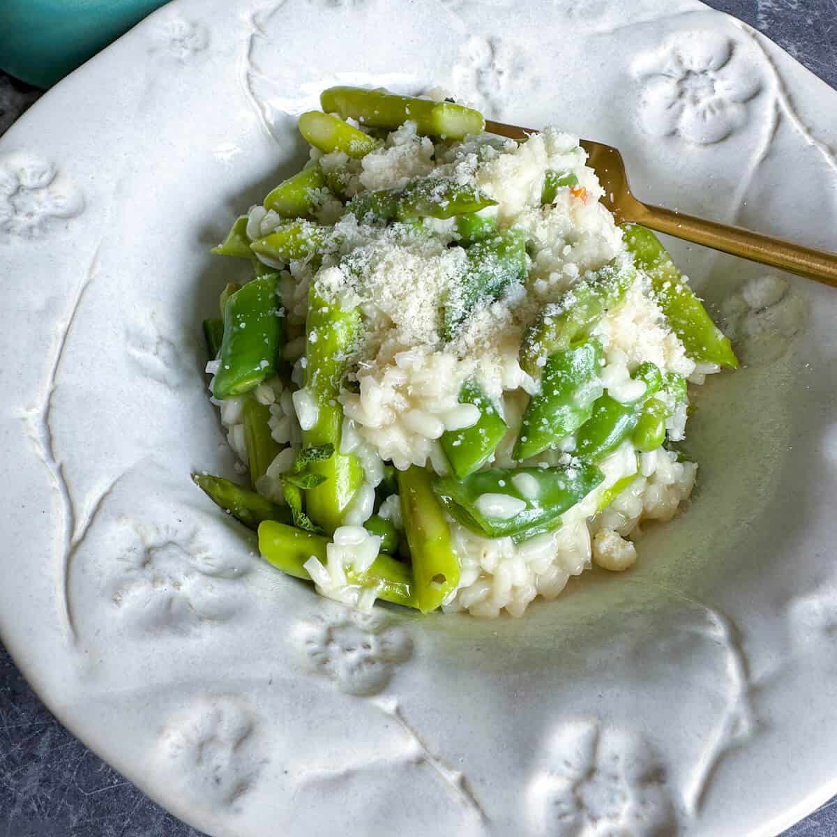 Risotto with asparagus and peas in a bowl with parmesan cheese sprinkled over the top. 