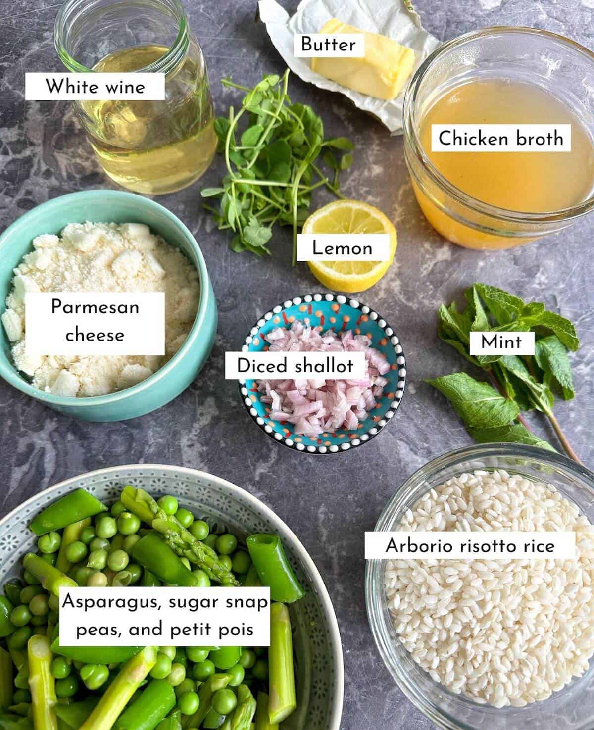 Ingredients for Spring risotto. Asparagus, peas, sugar snap peas, lemon, rice, broth, wine, parmesan cheese and mint on a worktop. 