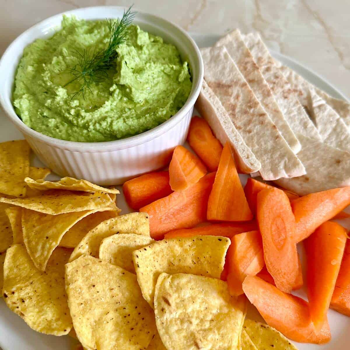 A plate of crudites, pitta, tortilla chips and green pea dip. 