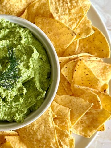 Easy green pea dip in a bowl surrounded by tortilla chips.