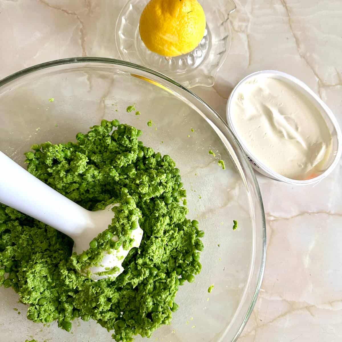 A bowl of pea puree with lemon and cream cheese beside it. 