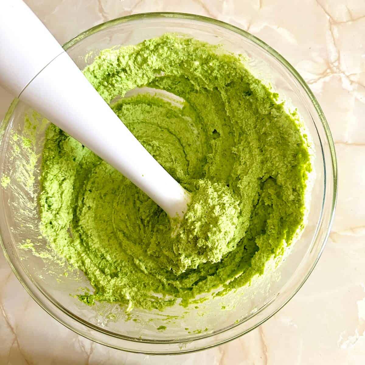 A bowl of blended green pea dip with an immersion blender. 