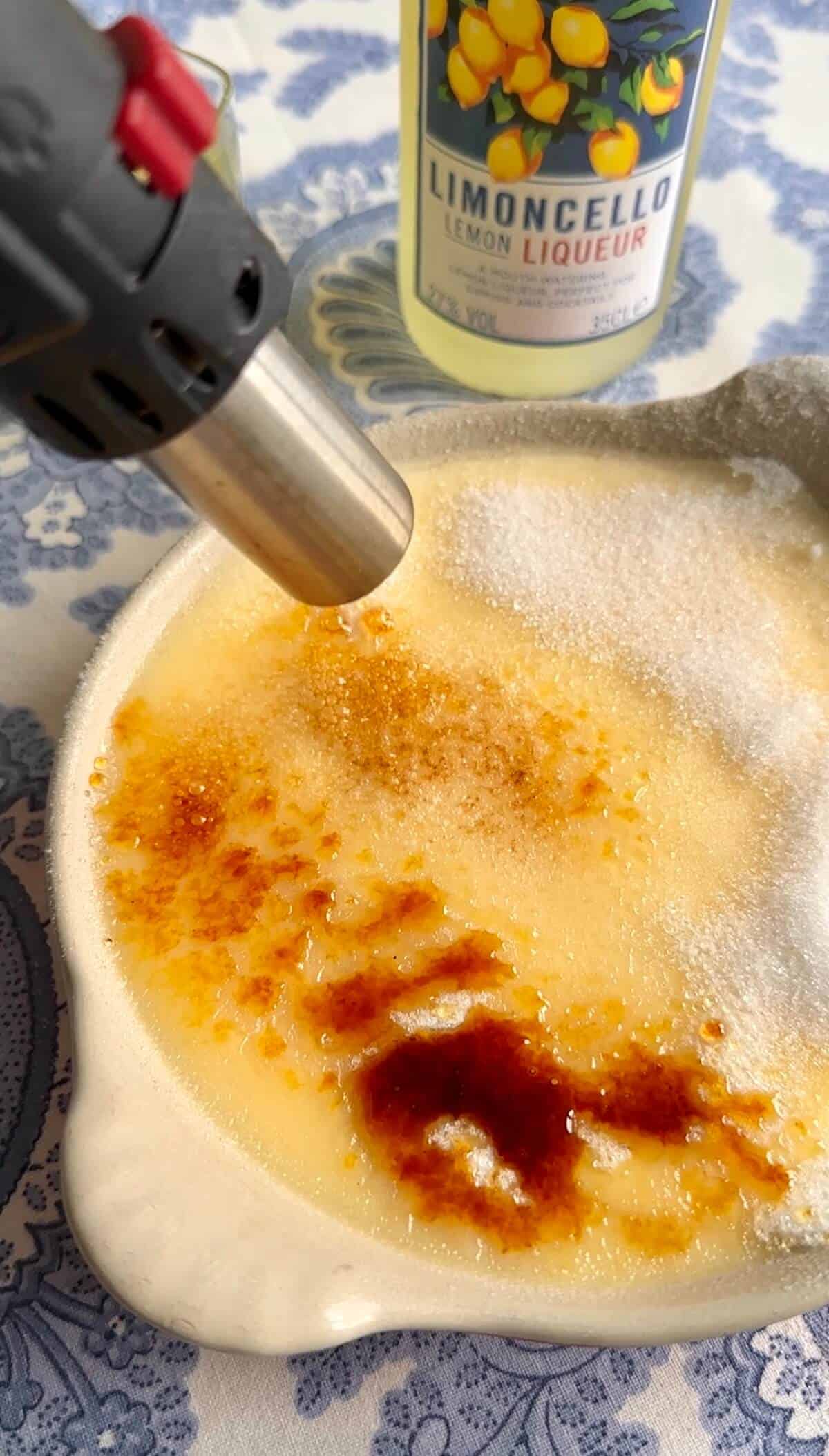 A kitchen torch bruleeing sugar on the surface of a Limoncello creme brulee. 