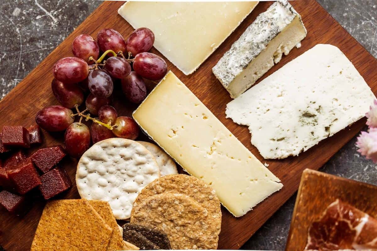 A cheeseboard with various different cheeses, grapes and crackers. 