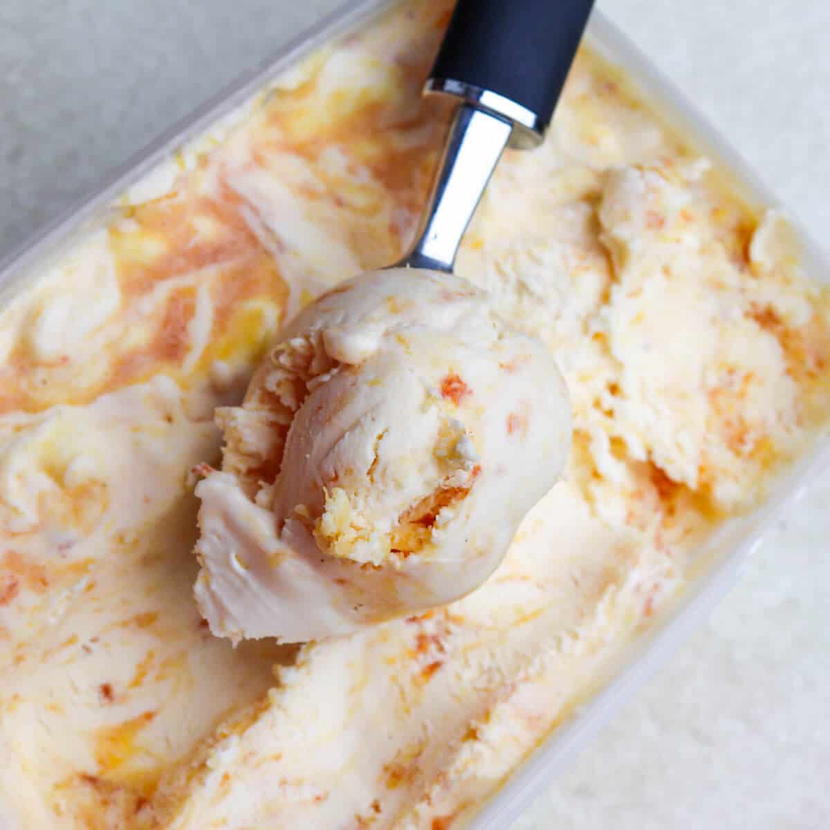 Peaches-and-cream-ice-cream-in-a-tub-with-ice-cream-scoop.