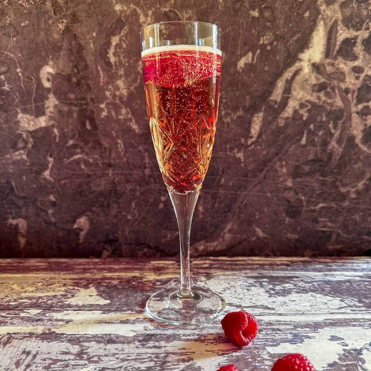 A classic Kir Royale cocktail garnished with a raspberry. 