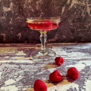 A classic Kir Royale champagne cocktail surrounded by fresh raspberries.