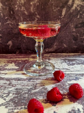 A classic Kir Royale champagne cocktail surrounded by fresh raspberries.
