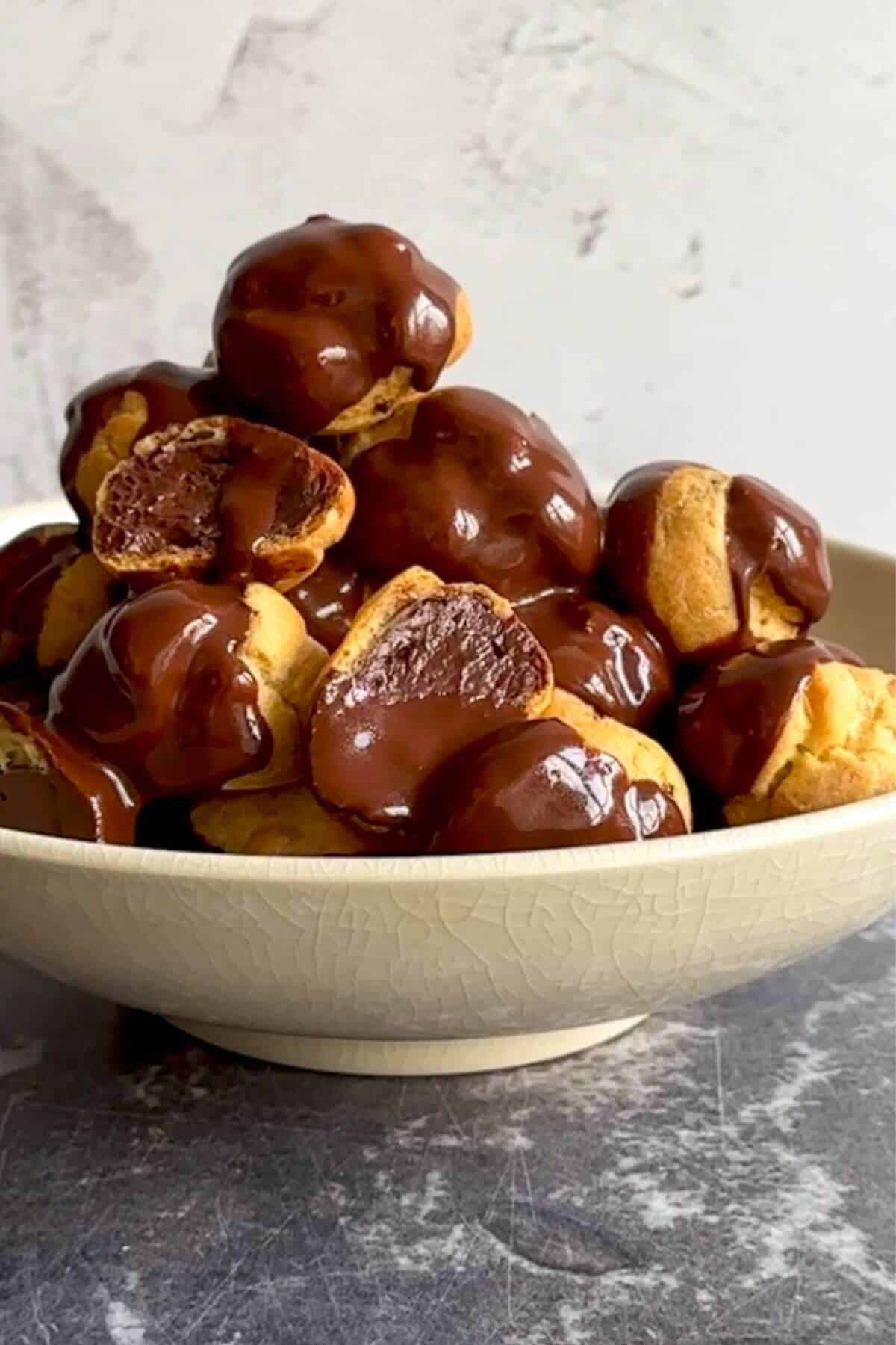 Classic profiteroles with chocolate truffle filling in a bowl, covered in chocolate sauce. 