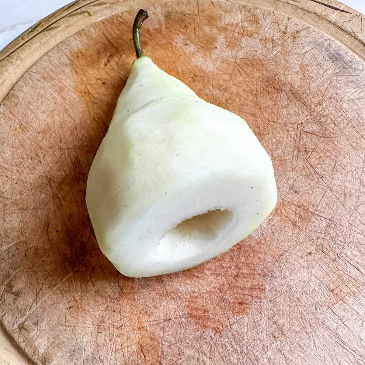 A peeled and cored pear on a chopping board.