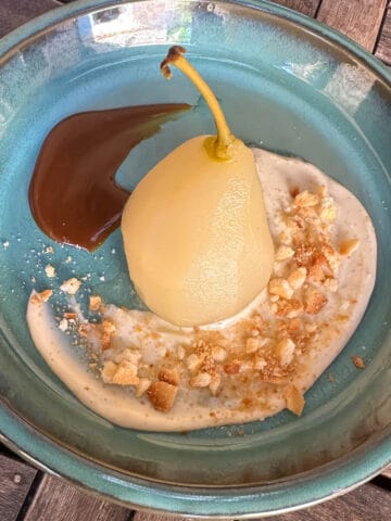 A poached pear on a plate with some cream and caramel sauce.