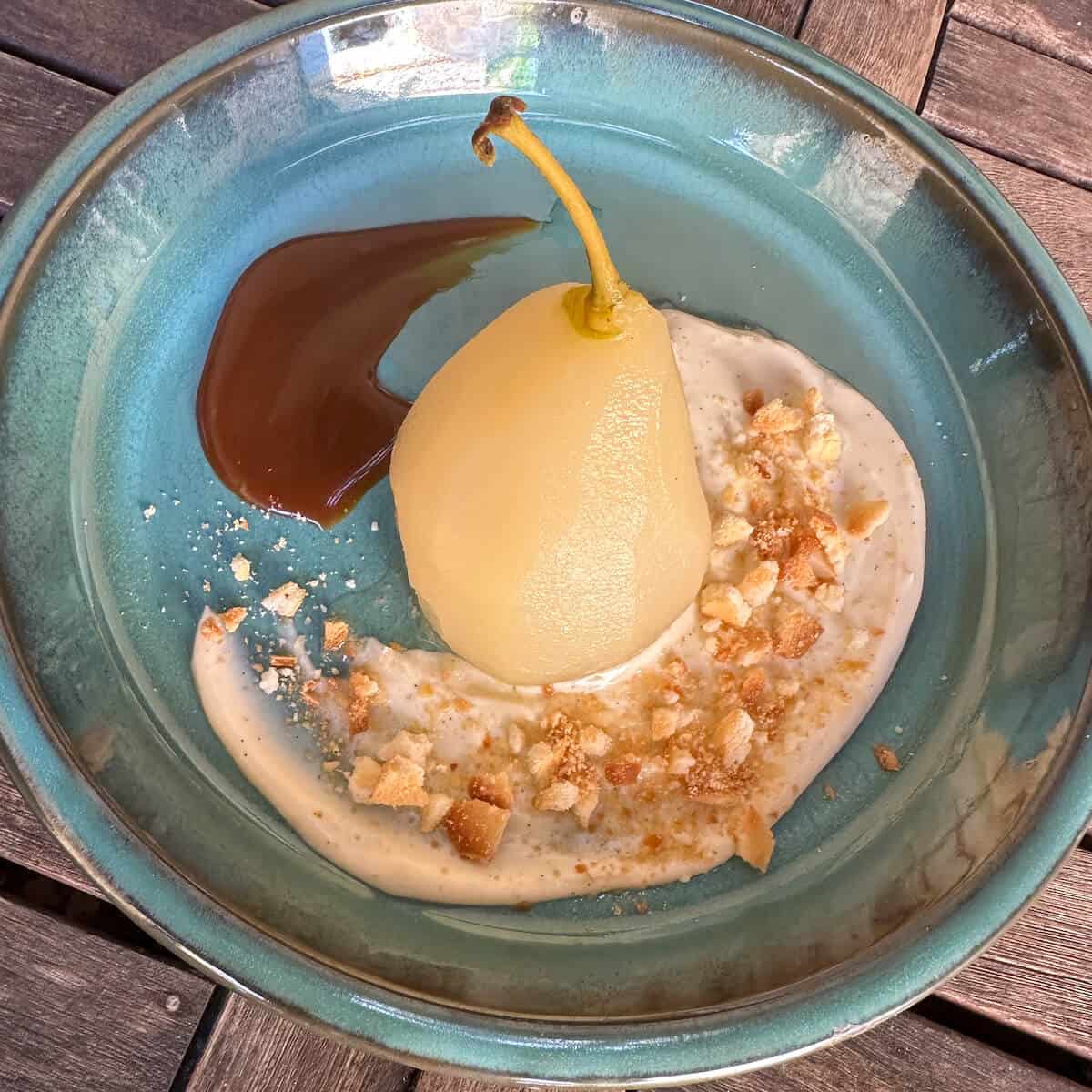 A poached pear on a plate with some cream and caramel sauce. 