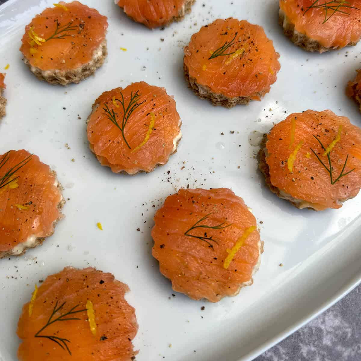 Smoked salmon canapes on a serving platter garnished with lemon zest and fresh dill. 