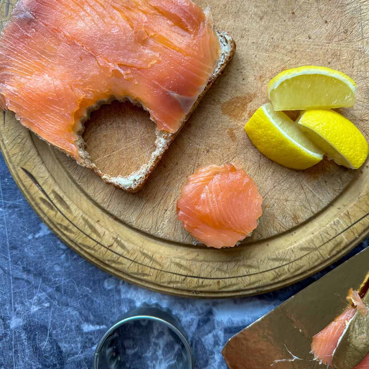 A circular smoked salmon canape cut out next to a piece of bread. 
