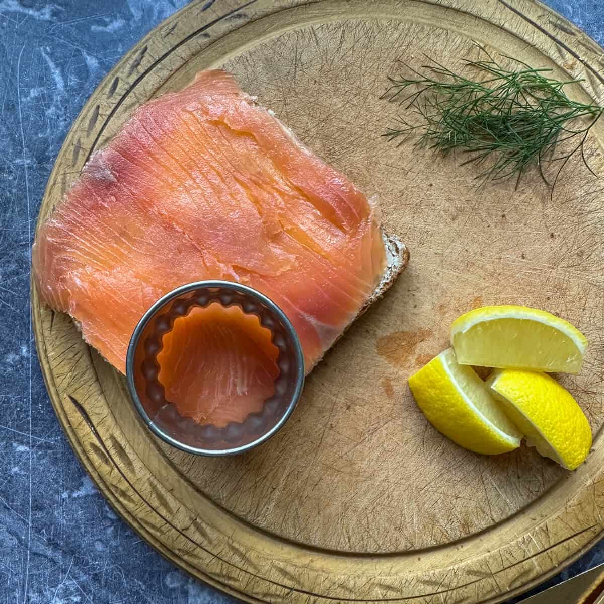 A round cookie cutter on top of a piece of bread and smoked salmon.