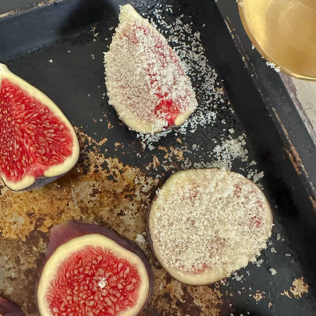 Figs covered in light brown sugar on a baking tray. 