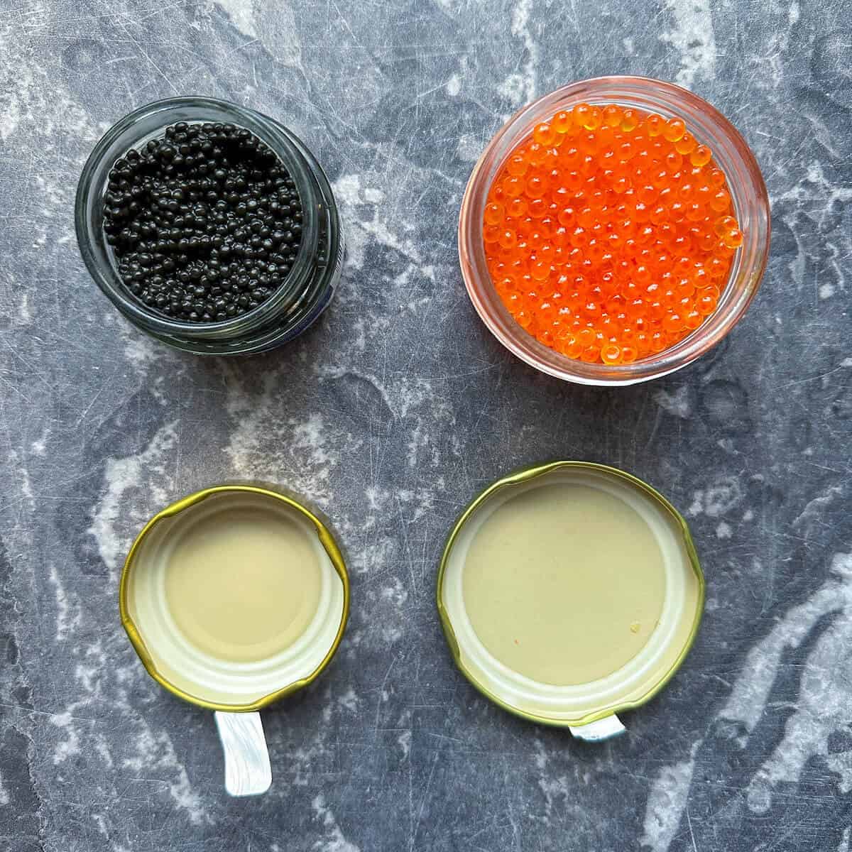 An open jar of caviar next to an open jar of salmon roe. 