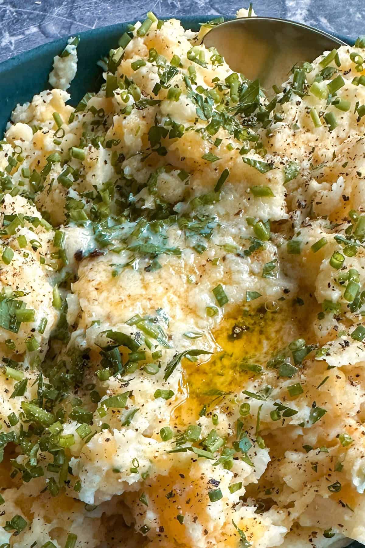 A close up of root vegetable mash covered in fresh green herbs and melted butter. 