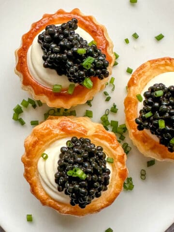 Caviar and creme fraiche vol au vents on a plate covered in chopped chives.