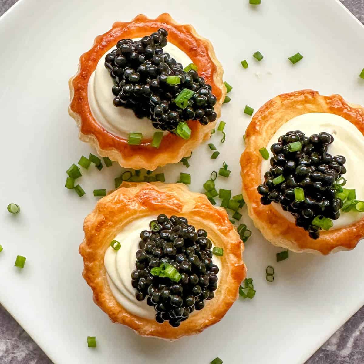 Caviar and creme fraiche vol au vents on a plate covered in chopped chives.