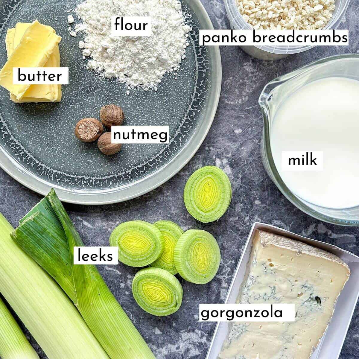 Ingredients for gorgonzola baked leeks on a table. Flour, butter, leeks, panko breadcrumbs, gorgonzola cheese, nutmeg and milk. 