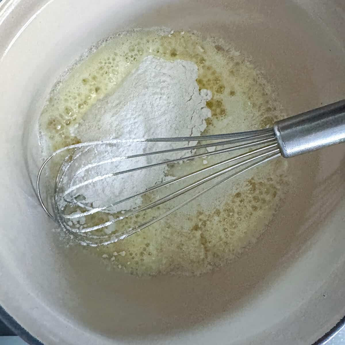 Melted butter and flour being whisked together in a saucepan to make a roux. 