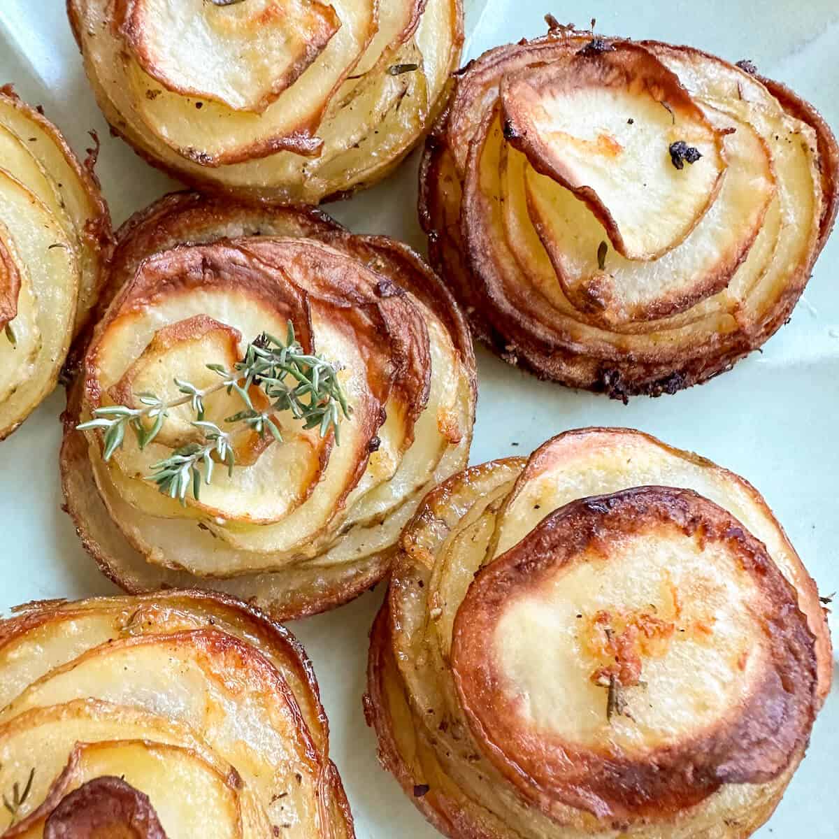 Baked crispy garlic potato roses on a plate with fresh thyme garnish. 