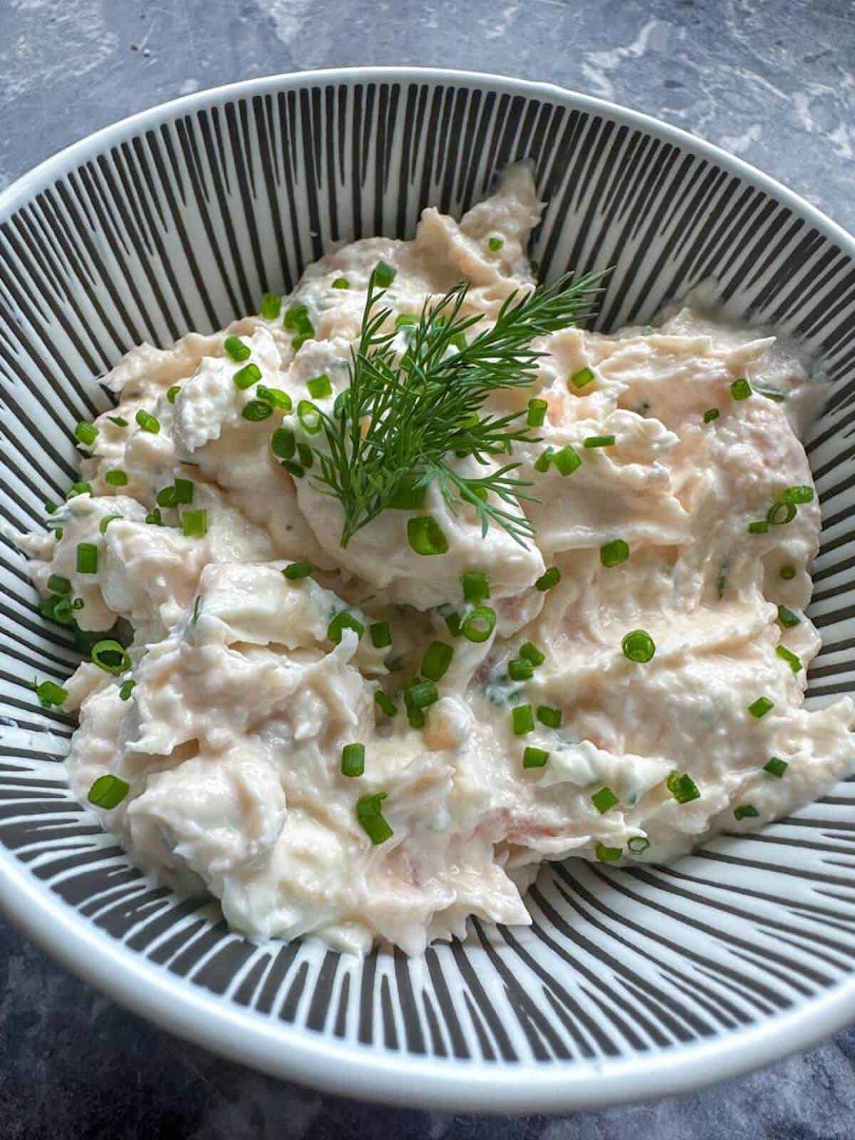 A close up of smoked salmon dip in a serving bowl garnished with fresh chives and dill.