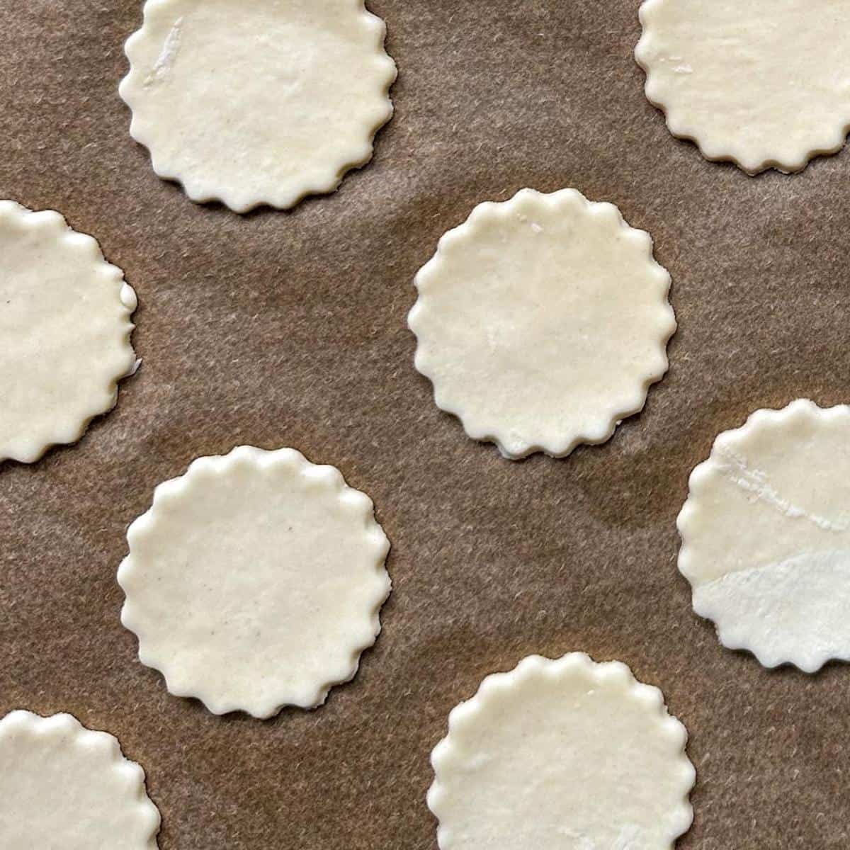 A lined baking sheet with cut out circles of puff pastry dough.