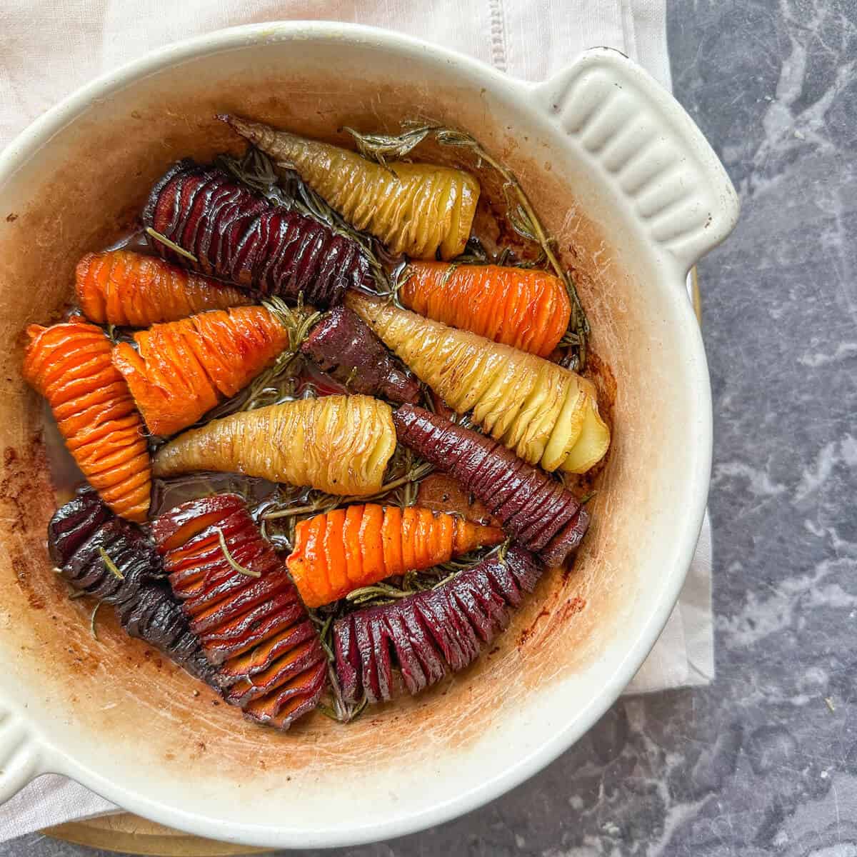 Roasted hasselback carrots with rosemary sprigs and honey glaze in an oven dish. 