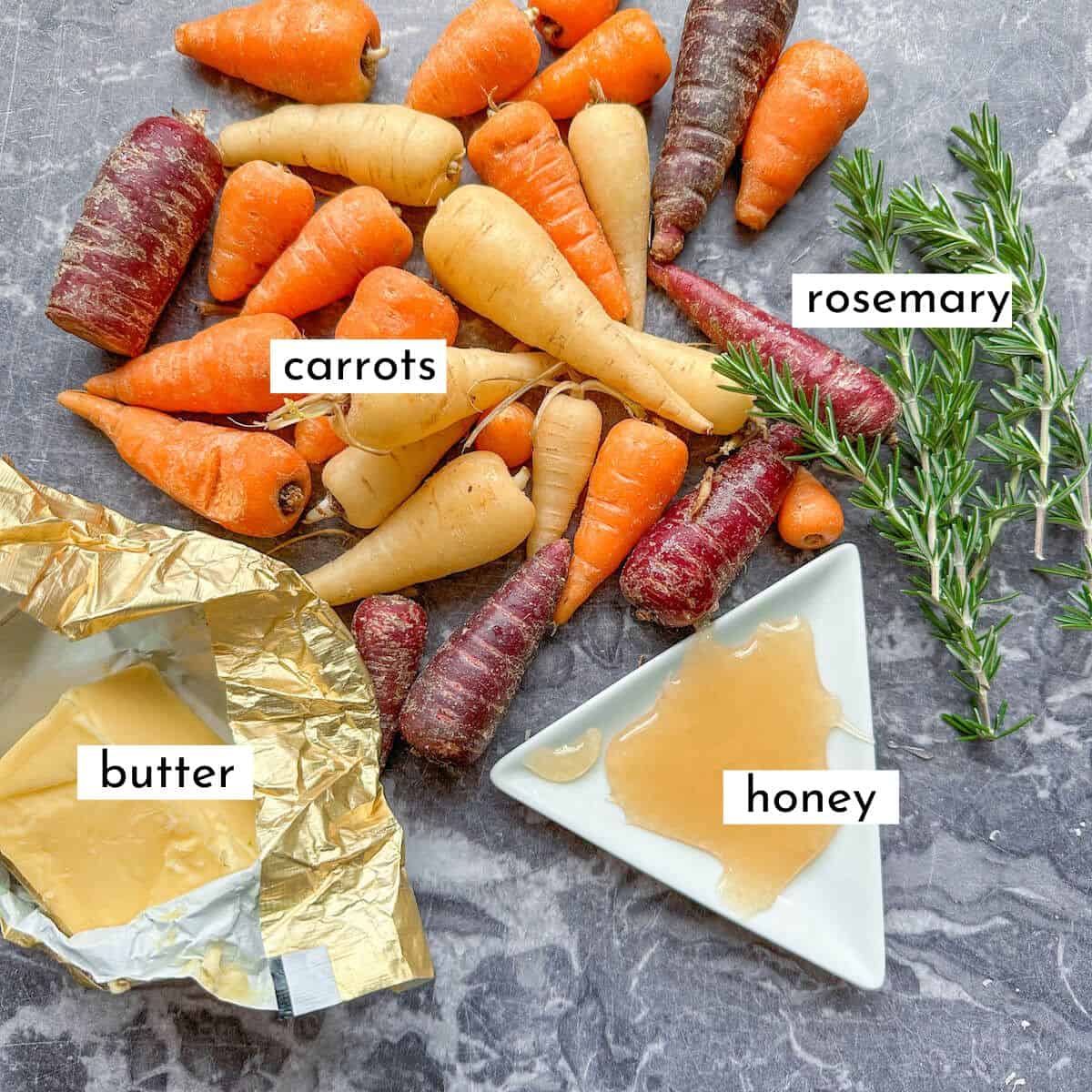 Ingredients for roasted hasselback carrots on a kitchen worktop. Carrots, rosemary, honey and butter. 