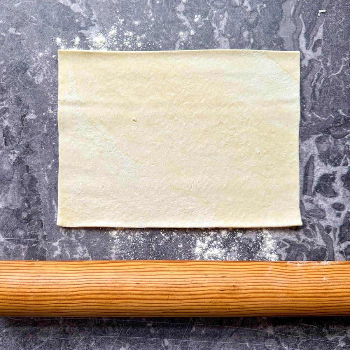 A rolling pin next to a piece of puff pastry.