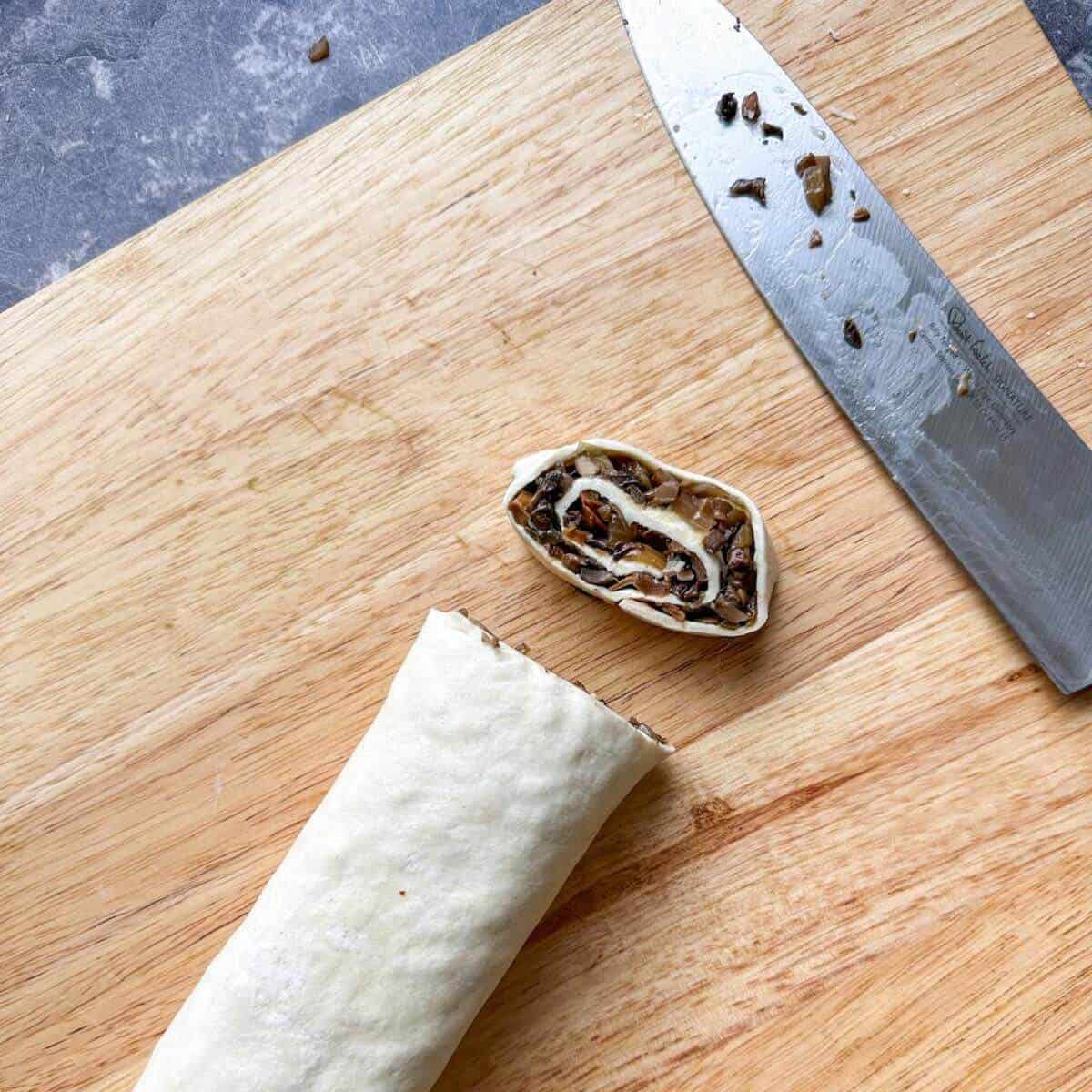 A chopping board with a knife and a log of puff pastry pinwheels. 