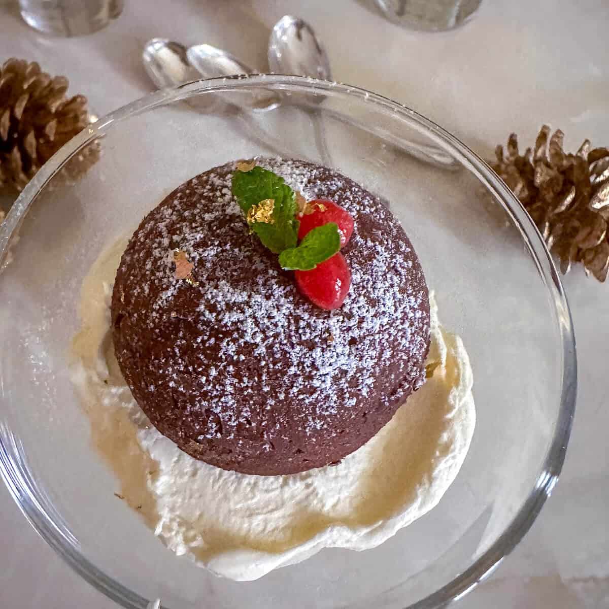 A serving of one chocolate truffle bomb in a glass dessert bowl with whipped cream. 
