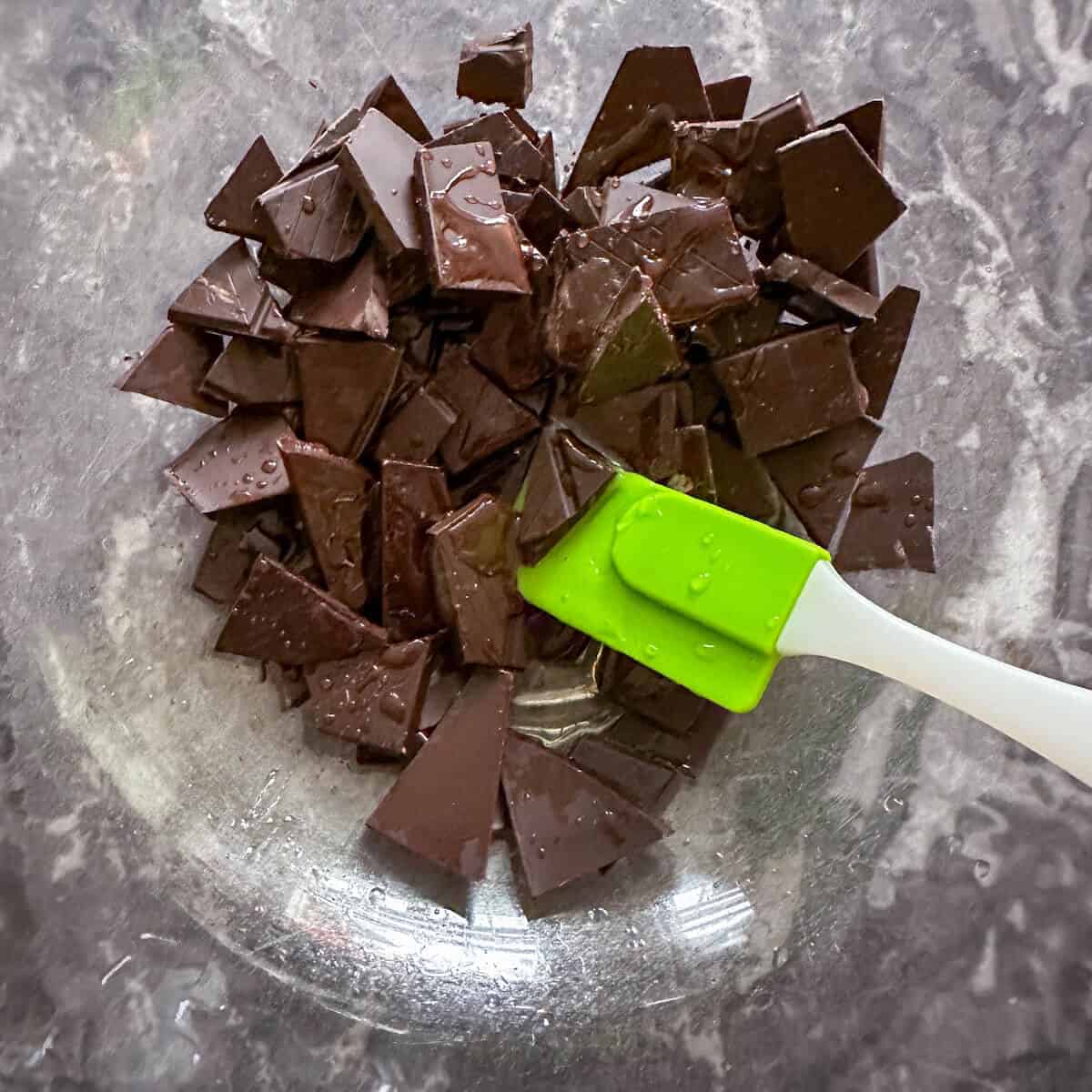 A broken up chocolate bar in a glass mixing bowl with liquid glucose. 