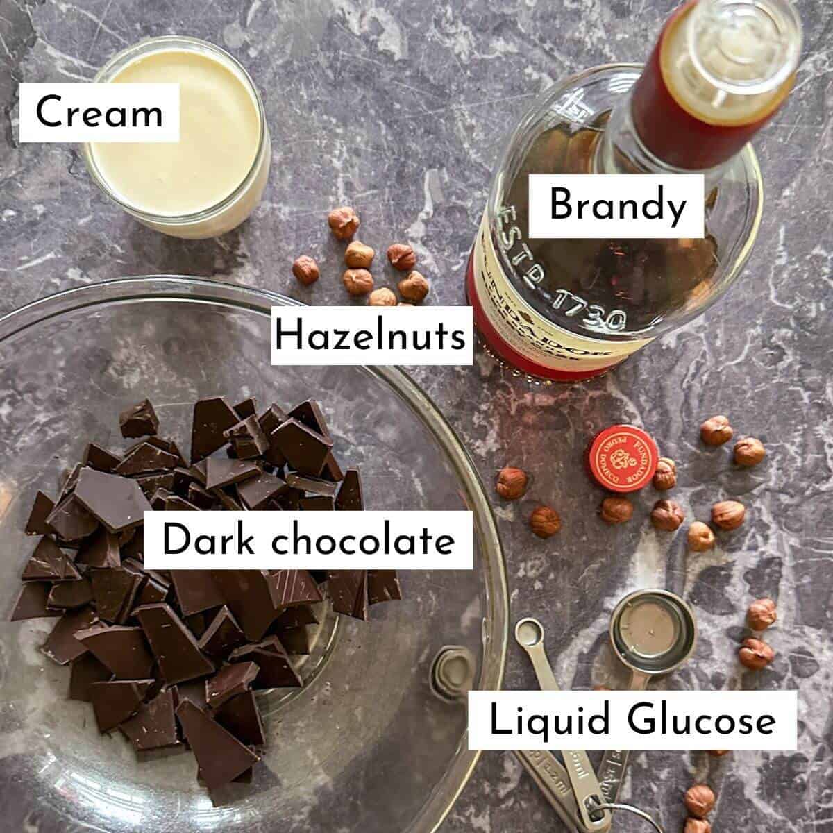 Ingredients on a worktop. Dark chocolate, cream, hazelnuts, brandy, and liquid glucose. 