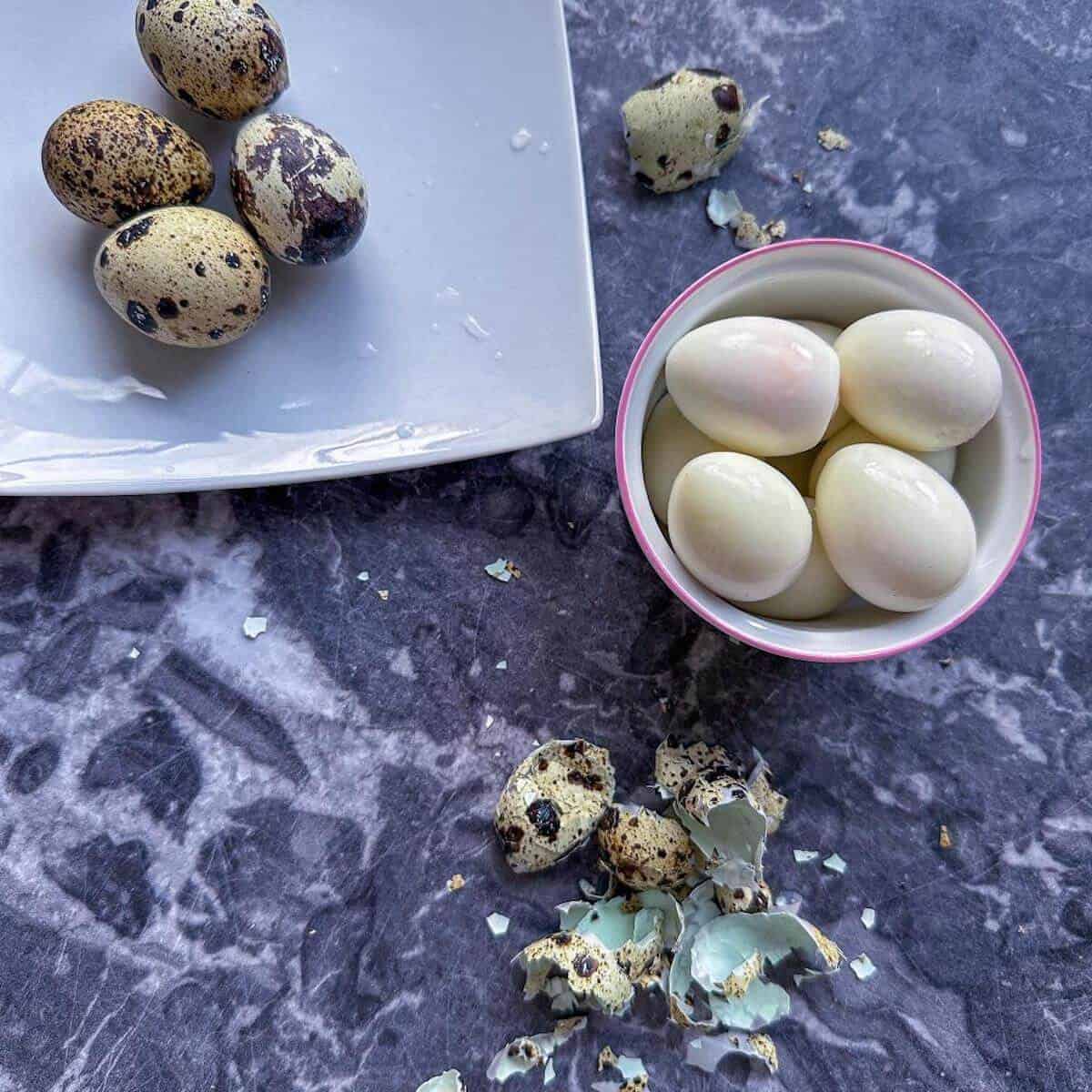 Some unpeeled and some peeled quails eggs on a worktop. 