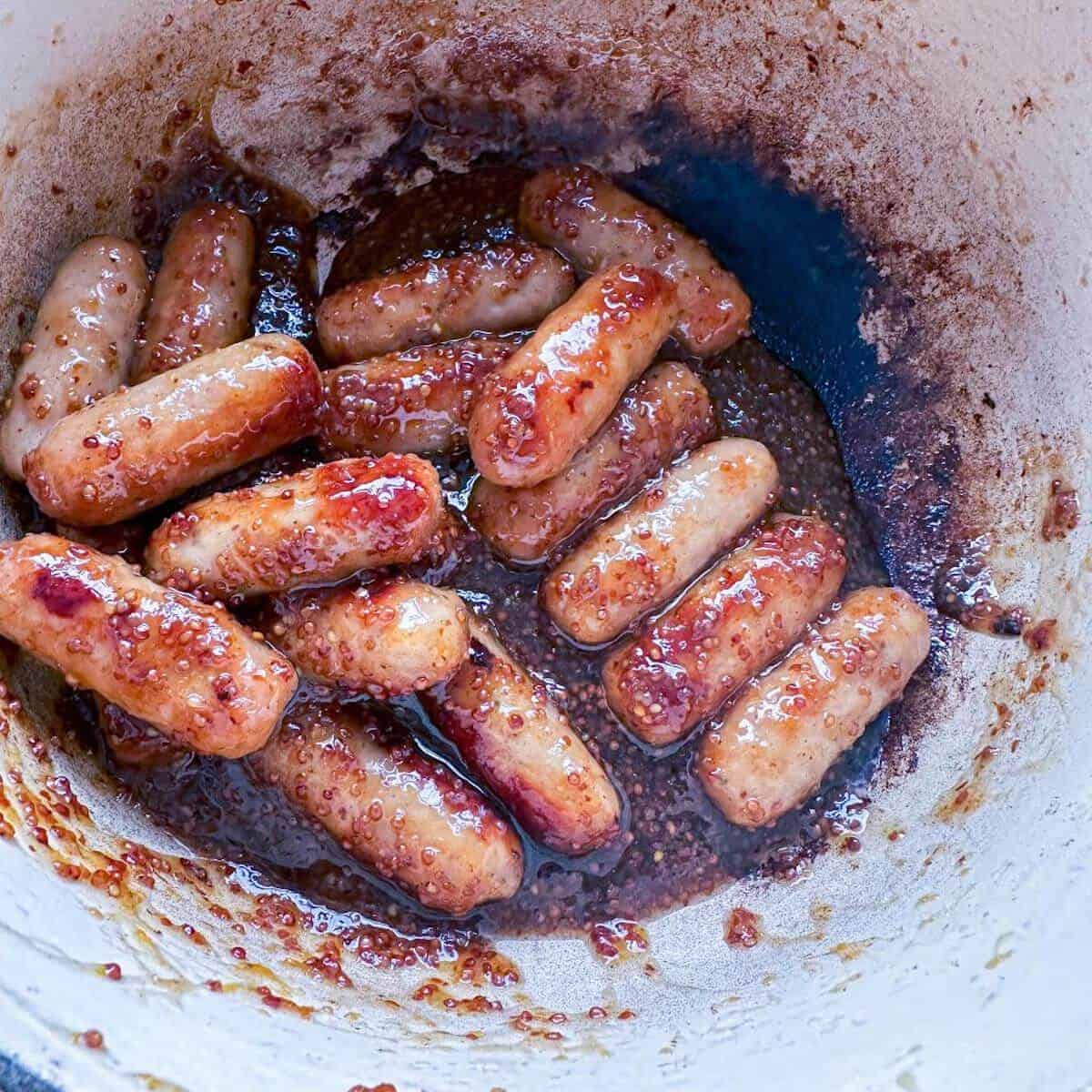 A casserole dish filled with cocktail sausages being cooked in a honey mustard glaze. 