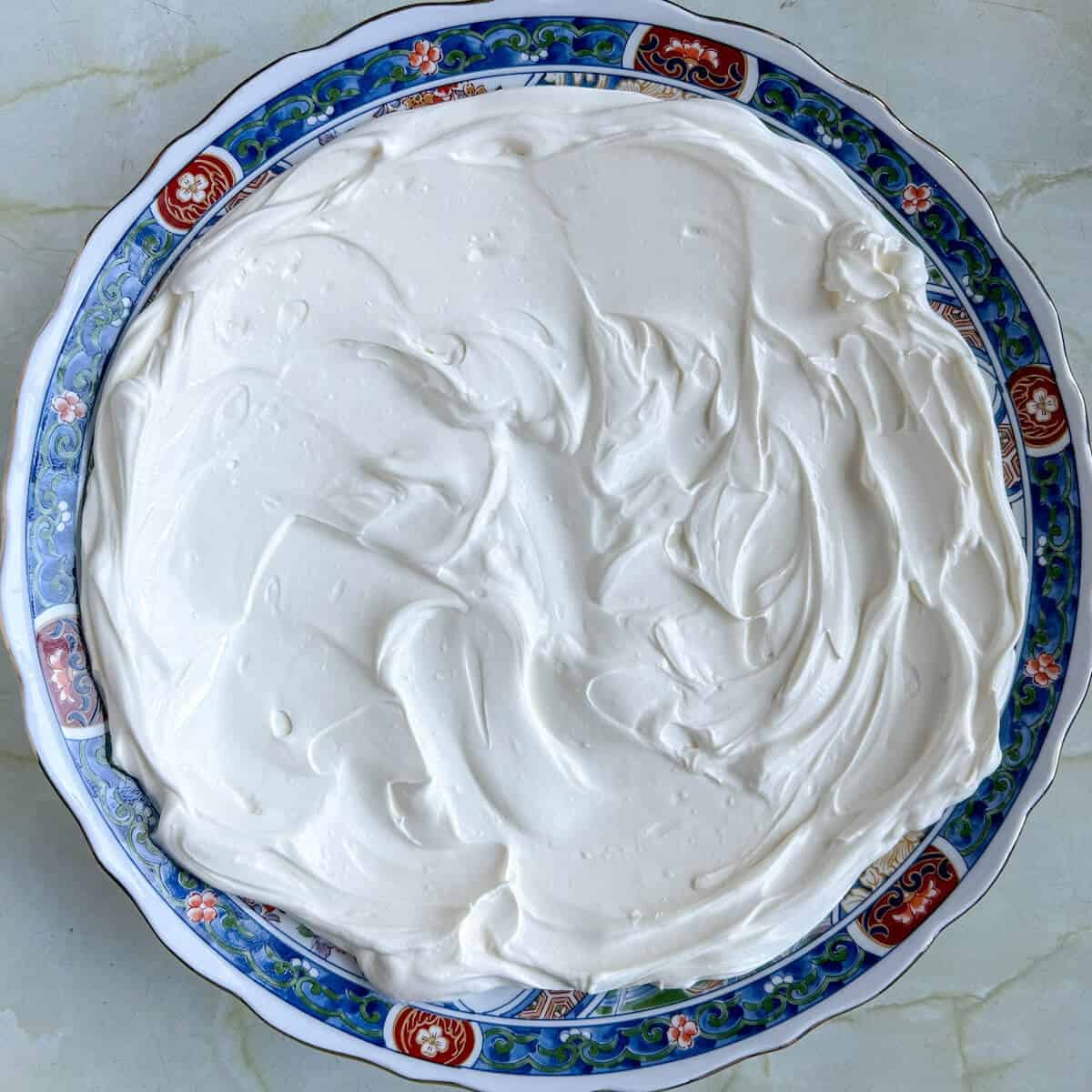 An ornate serving platter with cream cheese and sour cream dip spread over the surface. 