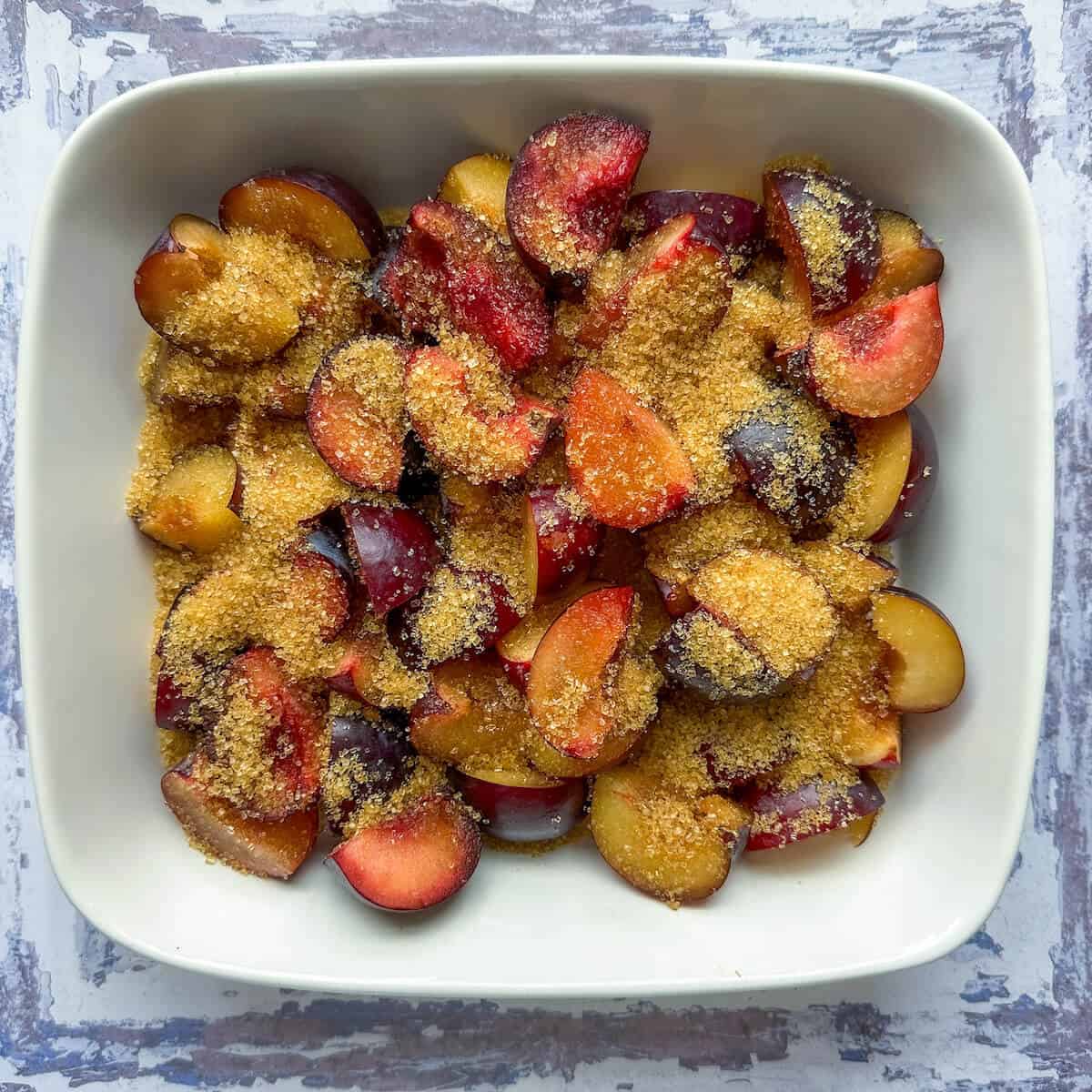 Quartered plums in a baking dish sprinkled with Demerara sugar. 
