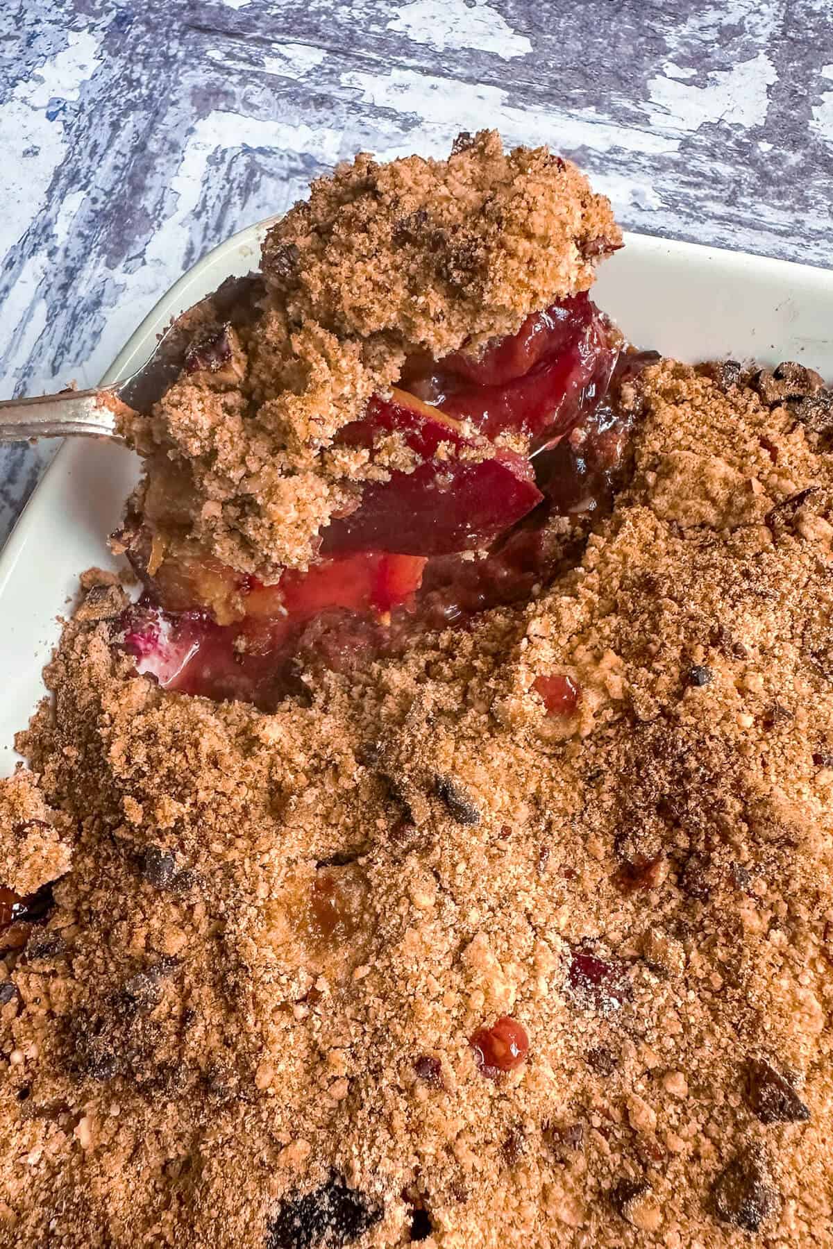 A serving of plum crumble being taken out with a big spoon. 