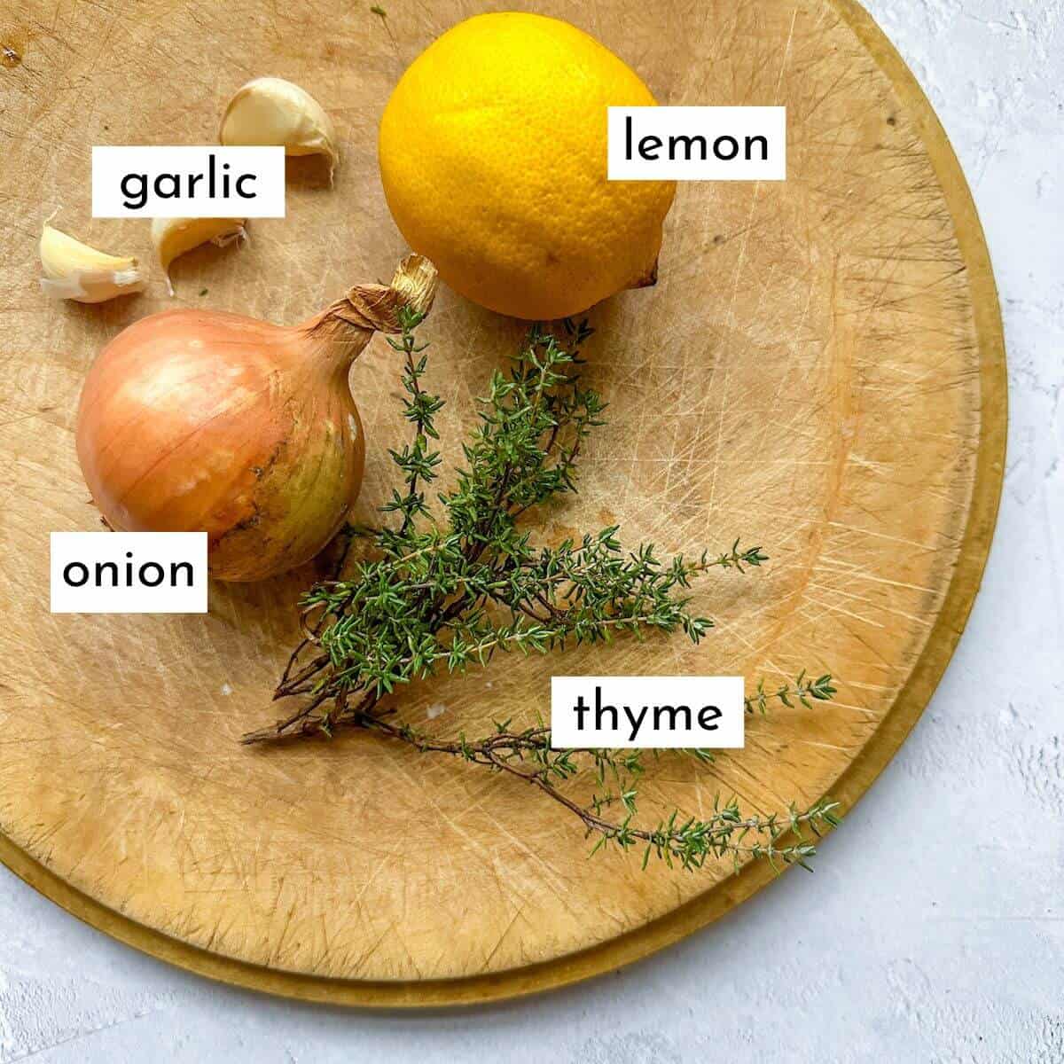 Lemon, garlic, thyme and onion on a chopping board.