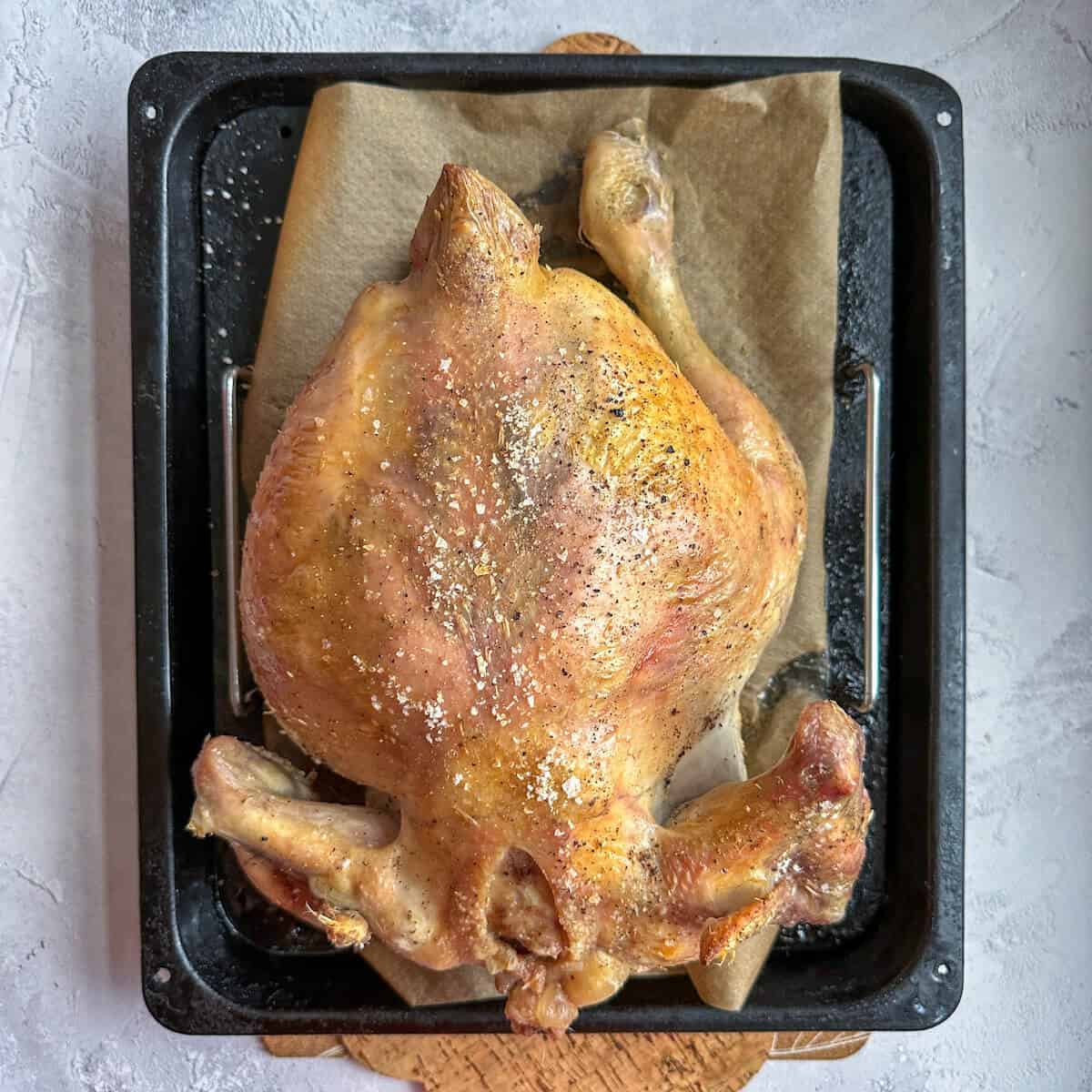 Capon chicken that is part cooked, upside down on a roasting tray. 