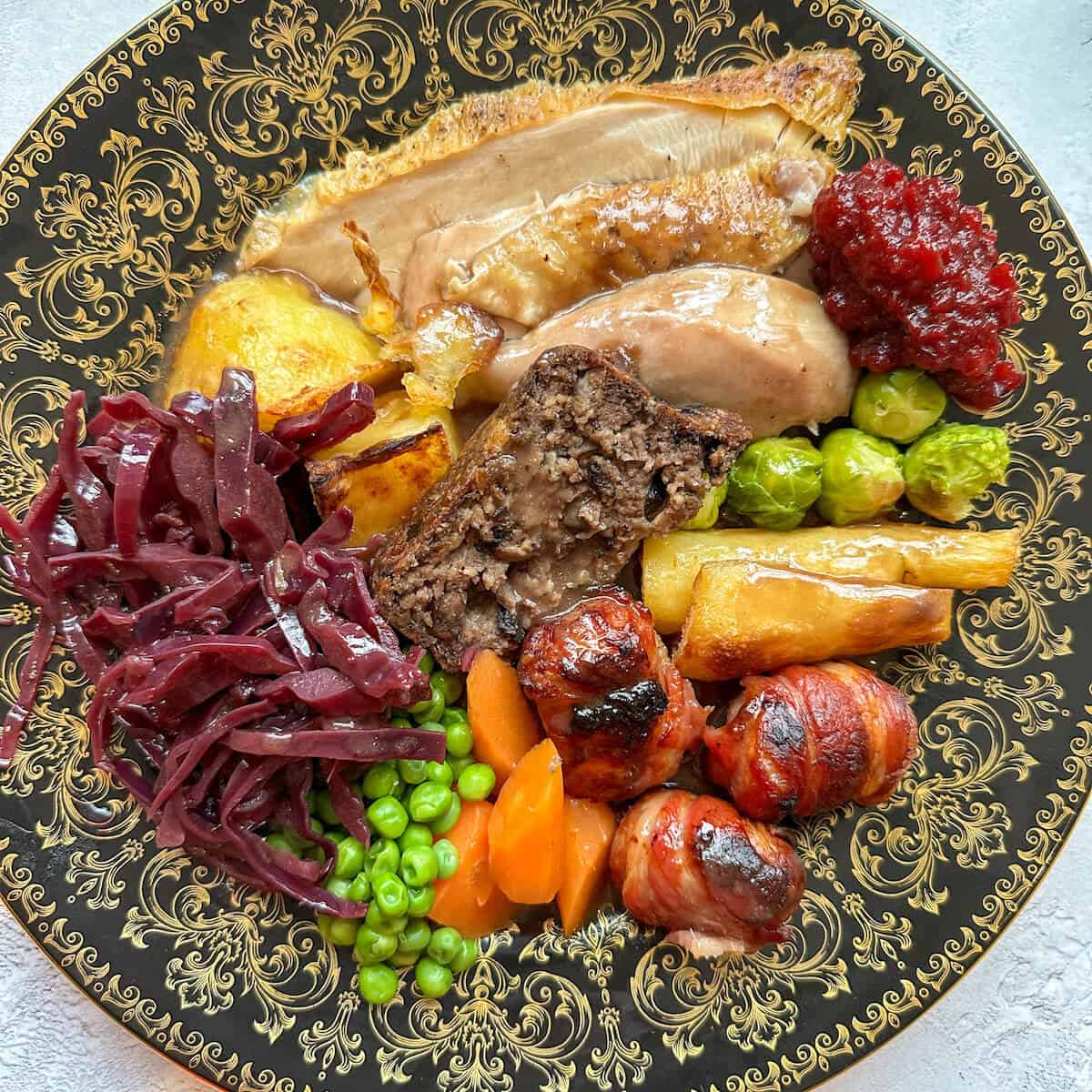 A plate of Christmas dinner full of capon chicken, red cabbage, parsnips, peas, stuffing, roast potatoes and gravy. 