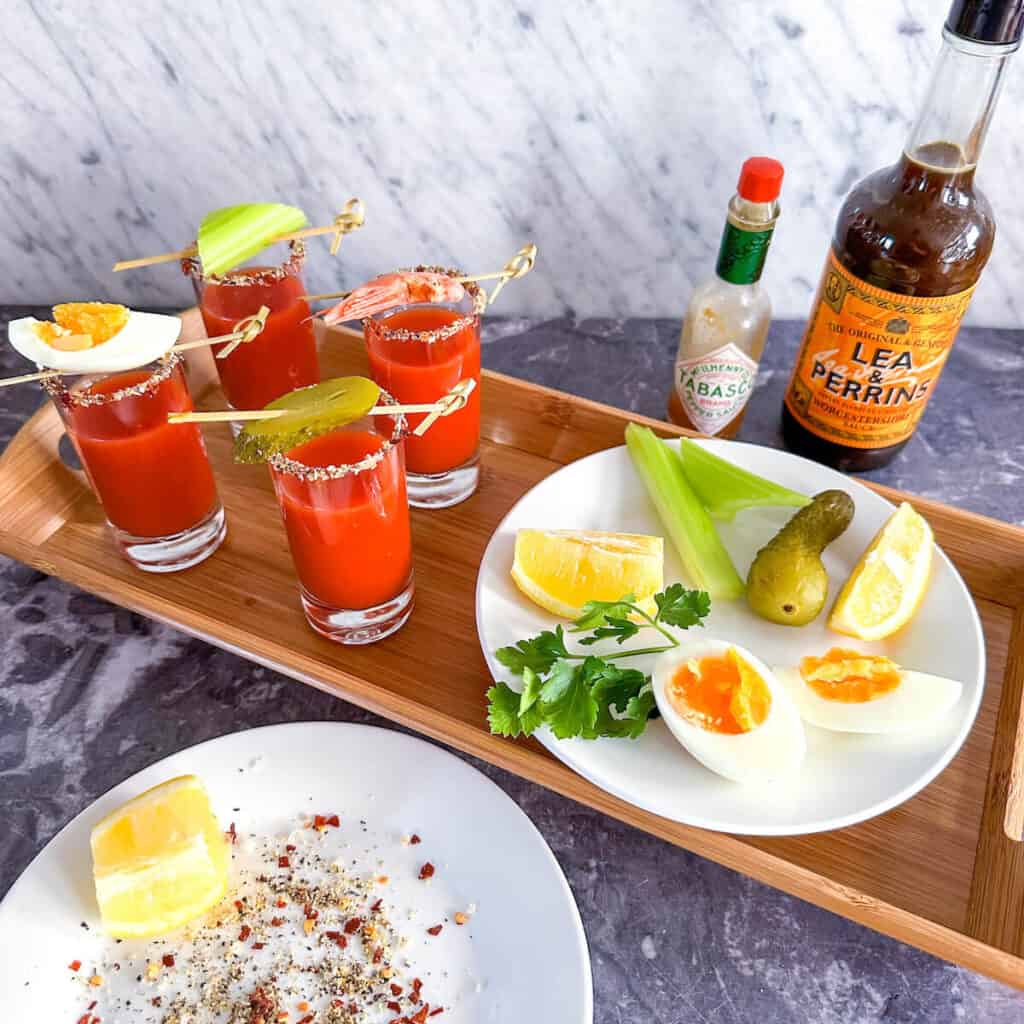 A tray of Bloody Mary amuse bouche shots next to a bottle of Tabasco and a bottle of Worcestershire sauce.