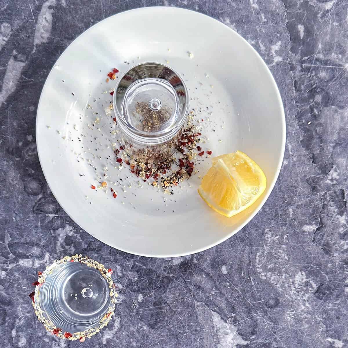 A shot glass being dipped into a plate of salt to make a rim. 