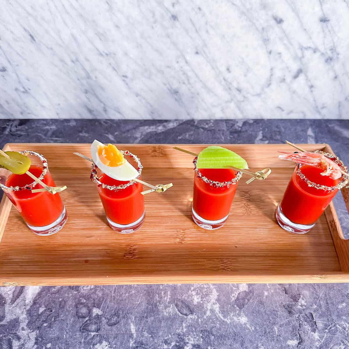 A tray with four shots of Bloody Mary amuse bouche on it. 