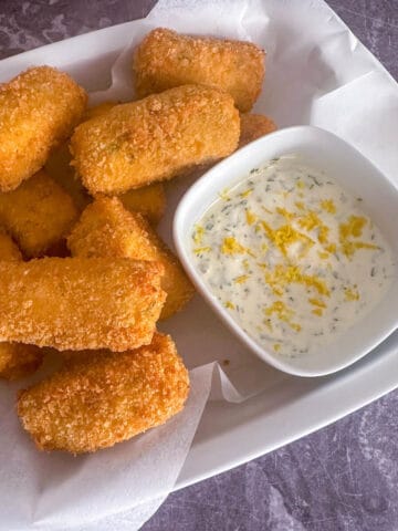 Crab croquettes in a lined serving dish with a bowl of lemon and herb mayonnaise.