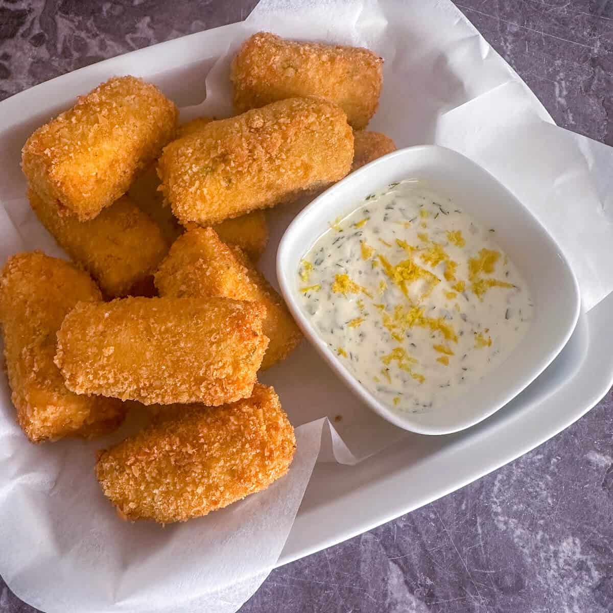 Crab croquettes in a lined serving dish with a bowl of lemon and herb mayonnaise. 